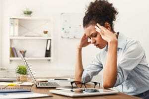 Lady sitting at desk holding head in her hands because she has a tension headache or migraine